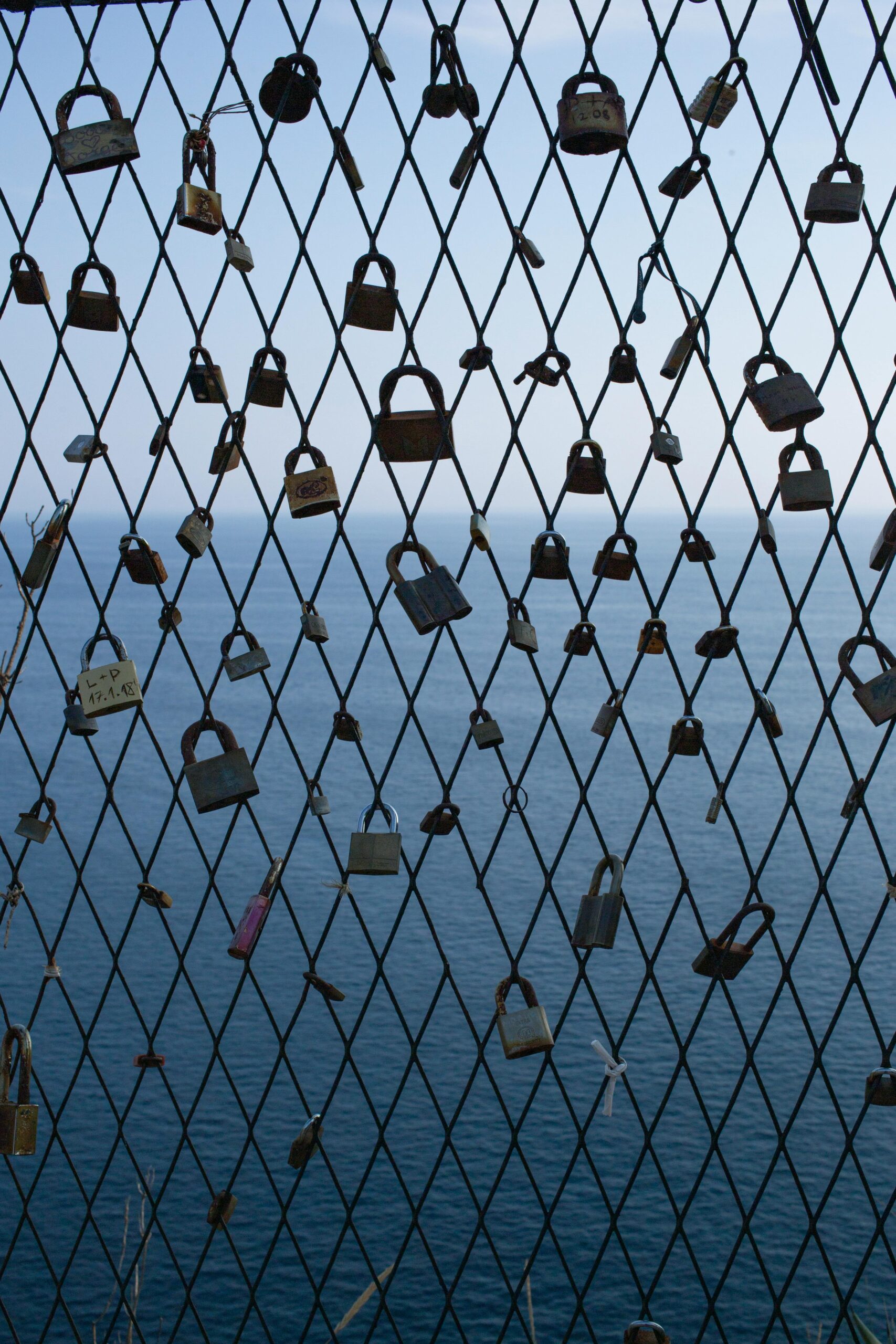 Padlocks on a fence in Dubrovnik with a serene Adriatic Sea backdrop, symbolizing love and commitment.